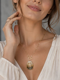 Woman wearing a gold necklace with a pendant, smiling softly.