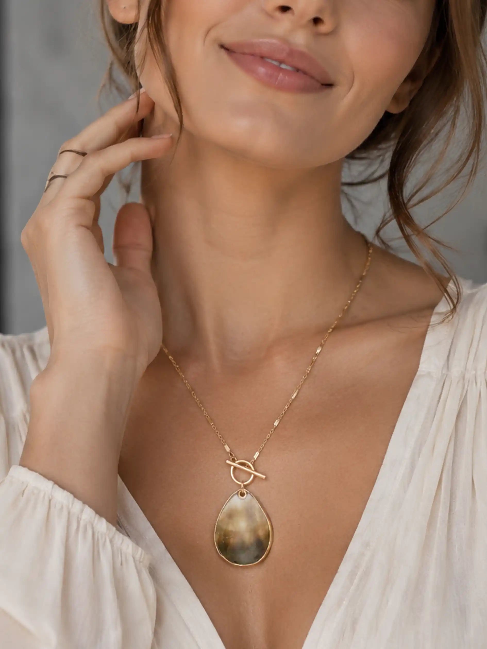 Woman wearing a gold necklace with a pendant, smiling softly.