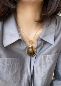 Person wearing a gold necklace with a large pendant on a light gray shirt.