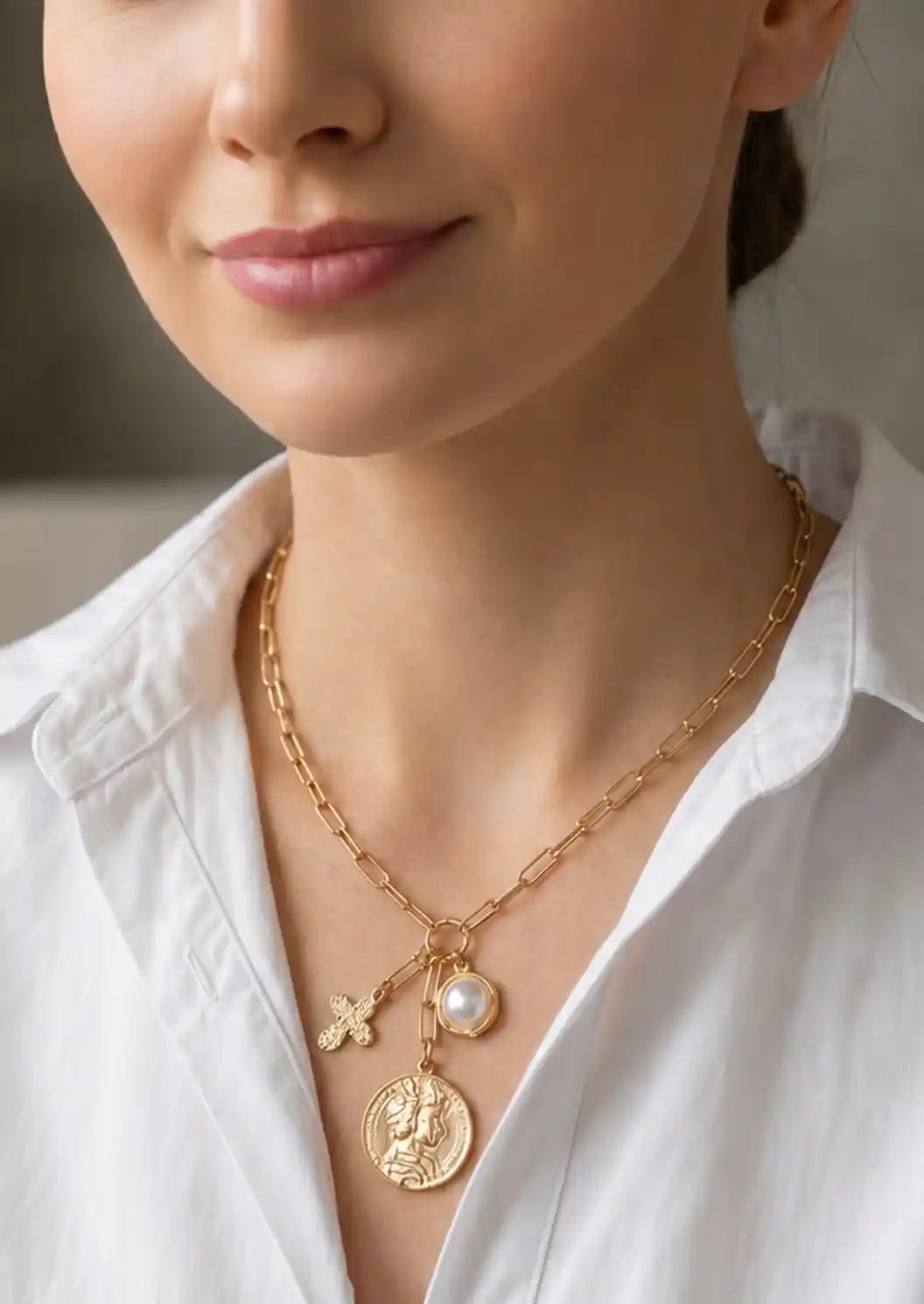 Close-up of a person wearing a gold necklace with charms on a blurred background
