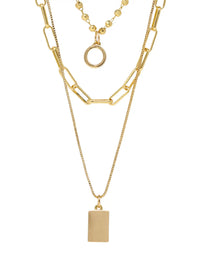A gold-toned three-layer necklace against a plain white background. The top layer features a short beaded chain with a simple circular ring pendant. The middle layer is a wider chain with elongated oval links. The bottom, longest layer is a fine chain with a solid rectangular bar pendant.