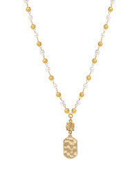 A gold-tone necklace featuring a beaded chain with alternating white pearls and gold beads, ending in a hammered gold pendant, shown on a plain white background.