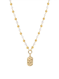 A delicate gold-tone necklace featuring a strand of alternating white pearls and small gold beads, with a hammered gold pendant shaped like a dog tag hanging from a gold ring.