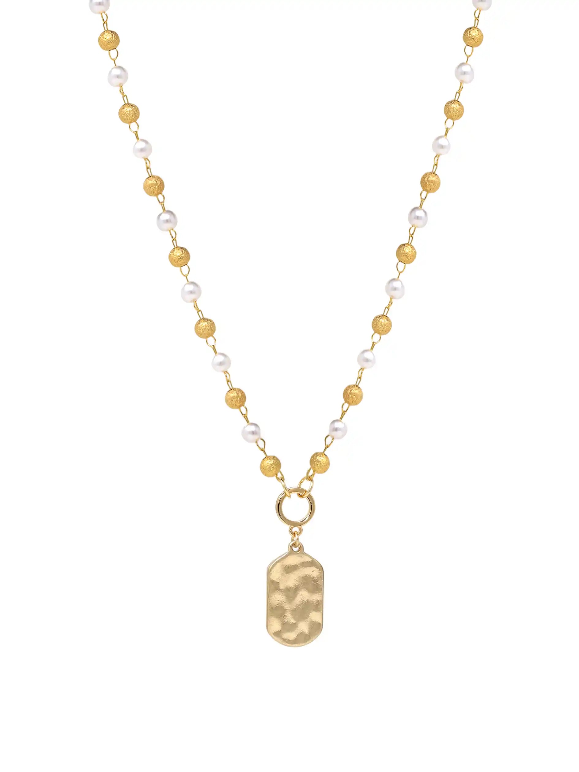 A delicate gold-tone necklace featuring a strand of alternating white pearls and small gold beads, with a hammered gold pendant shaped like a dog tag hanging from a gold ring.