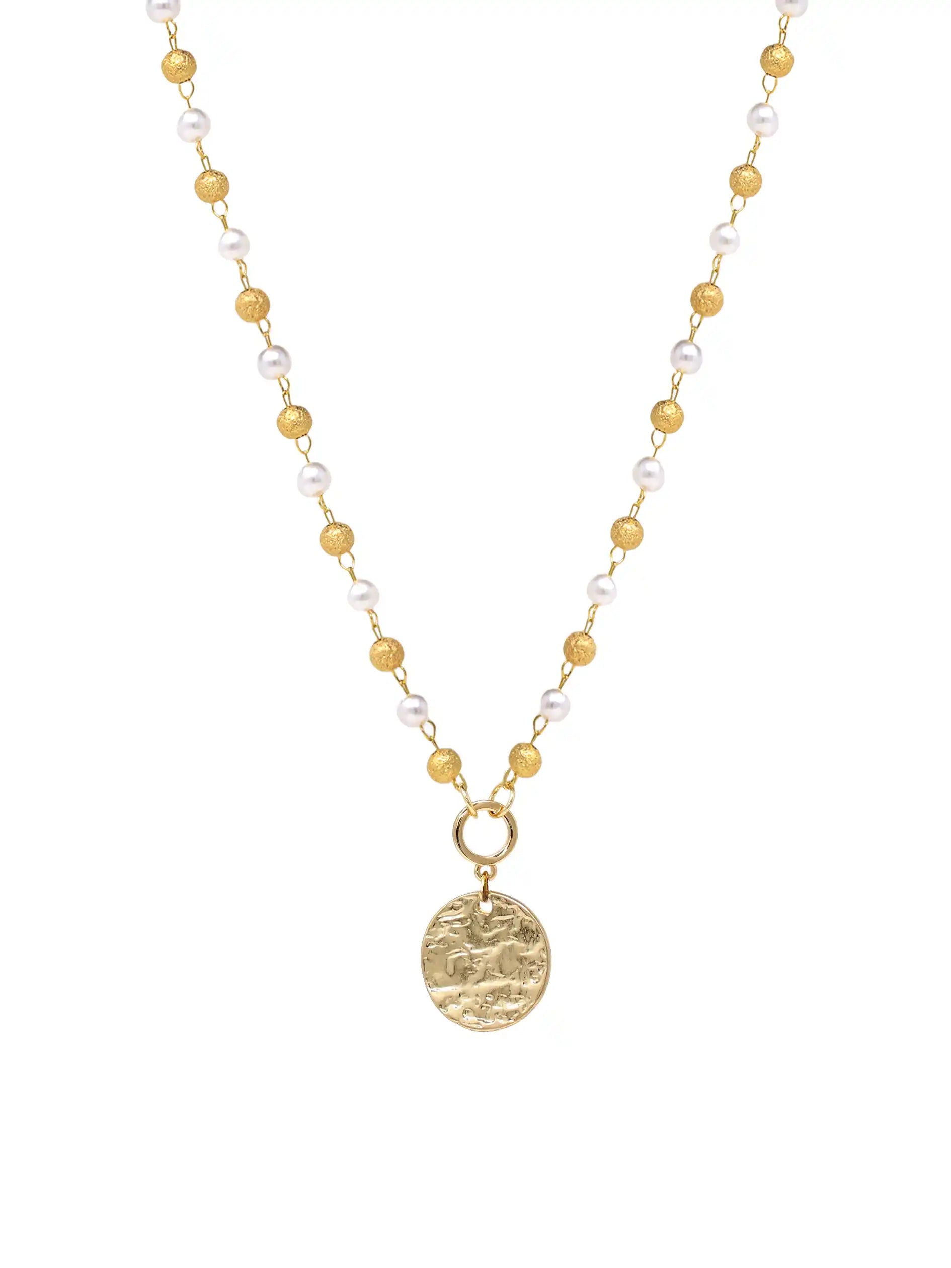 A delicate necklace featuring alternating white pearls and small gold beads on a gold chain, with a textured gold oval coin pendant hanging from a gold ring.