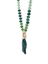 A beaded necklace featuring green and teal glass beads transitioning into a polished dark teal stone pendant, suspended from a gold-toned clasp on a white background.