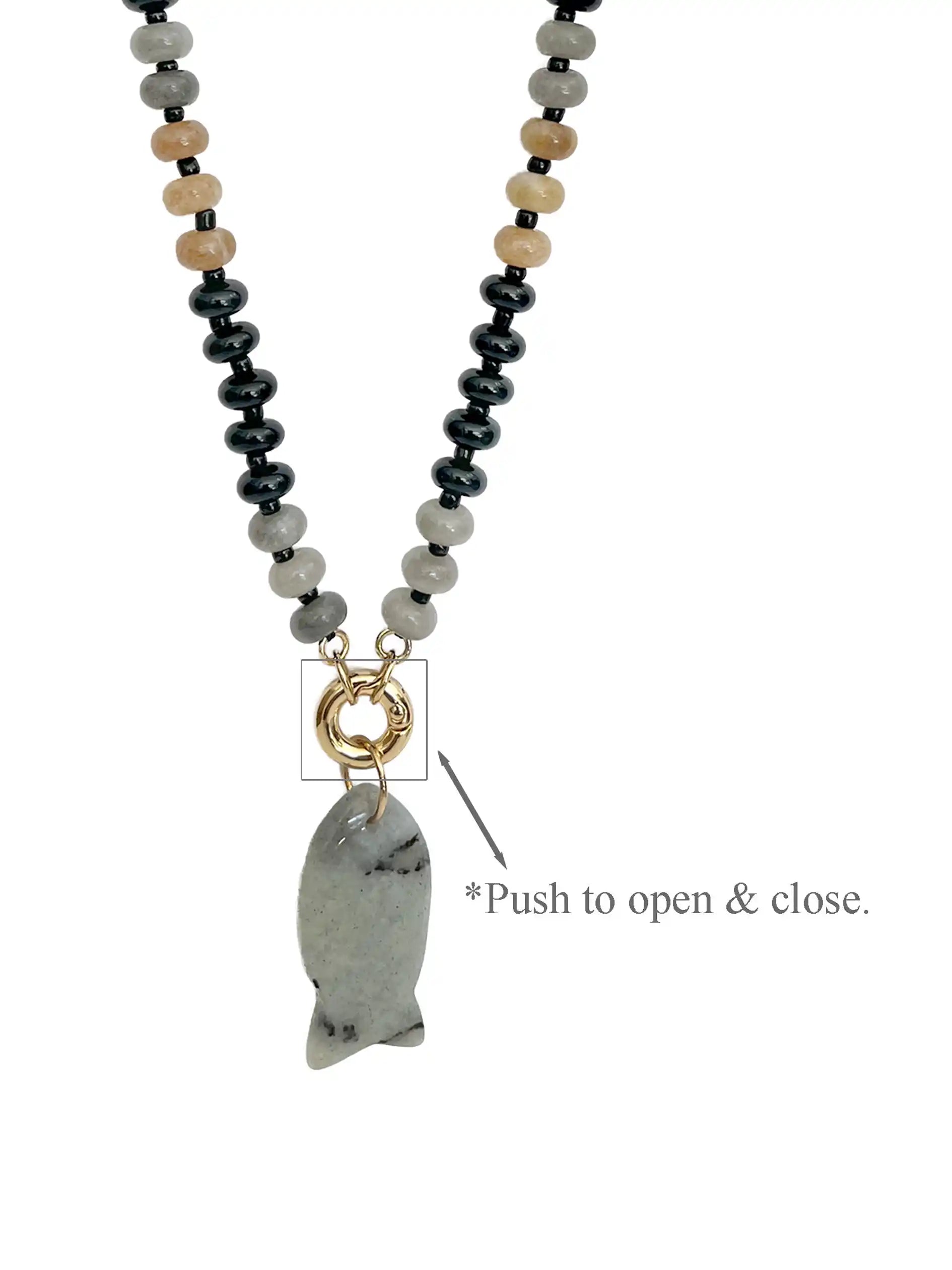 A beaded necklace with black, gray, and beige round beads, featuring a gold-tone ring clasp and a fish-shaped gray stone pendant. A text overlay explains how to open and close the clasp.