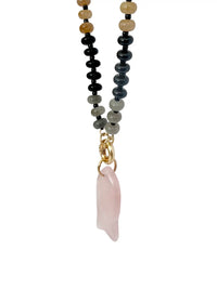 A beaded necklace featuring a dual-strand design with black and gray beads on one side, and light tan beads on the other, ending in a gold clasp and a pink rose quartz pendant, shown against a plain white background.