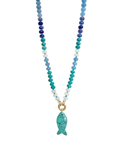 A beaded necklace featuring a gradient of blue, teal, and white beads, with a gold-tone ring clasp and a turquoise fish-shaped pendant with black veining, shown against a plain white background.