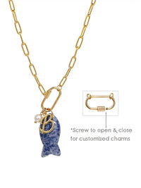 A gold paperclip chain necklace featuring a front-facing carabiner clasp that holds three distinct charms: a small round pearl, a gold script initial B, and a carved blue sodalite fish pendant.