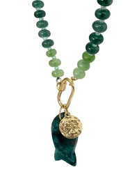 A beaded necklace featuring green and dark teal gemstone beads with a gold-tone carabiner clasp, hanging from a gold chain, and ending in a dark green stone pendant with a textured gold disc charm, shown on a plain white background.
