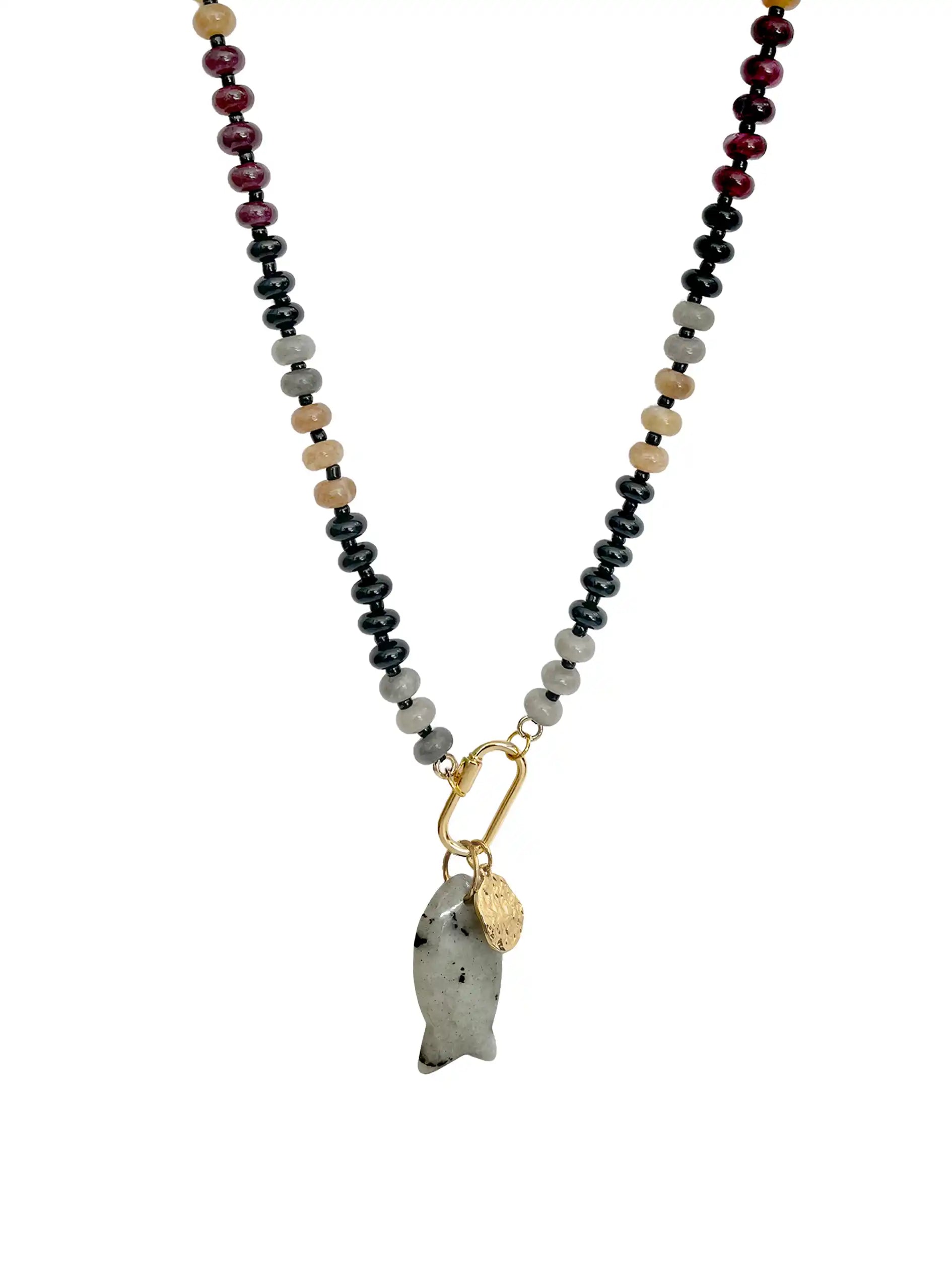 A beaded necklace featuring a central gold carabiner holding a polished gray stone fish pendant and a small gold tag, with the chain extending to the top edge. The chain itself is composed of alternating beads of black, light gray, tan, and deep burgundy on a plain white background.
