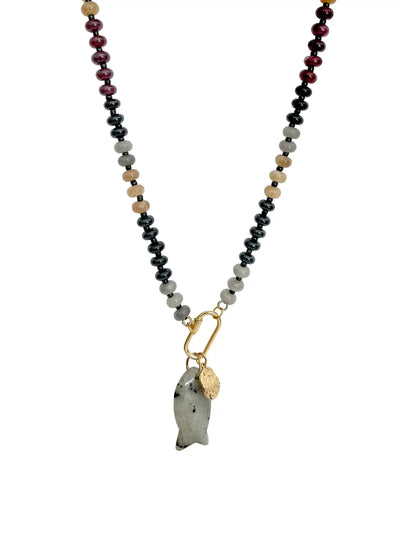 A beaded necklace featuring a central gold carabiner holding a polished gray stone fish pendant and a small gold tag, with the chain extending to the top edge. The chain itself is composed of alternating beads of black, light gray, tan, and deep burgundy on a plain white background.
