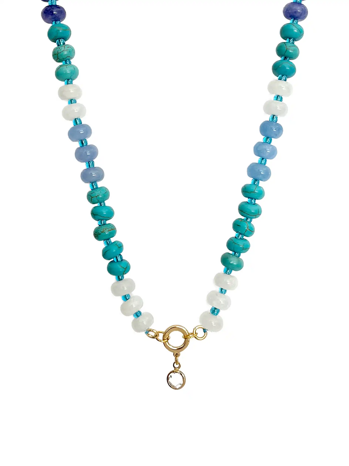A top-down photograph of a unique handmade semi-precious stone beaded necklace against a white background. The necklace features alternating deep blue, turquoise, light blue, and white stone beads. At the center is a gold-colored round ring with a small, clear crystal point pendant hanging from it.