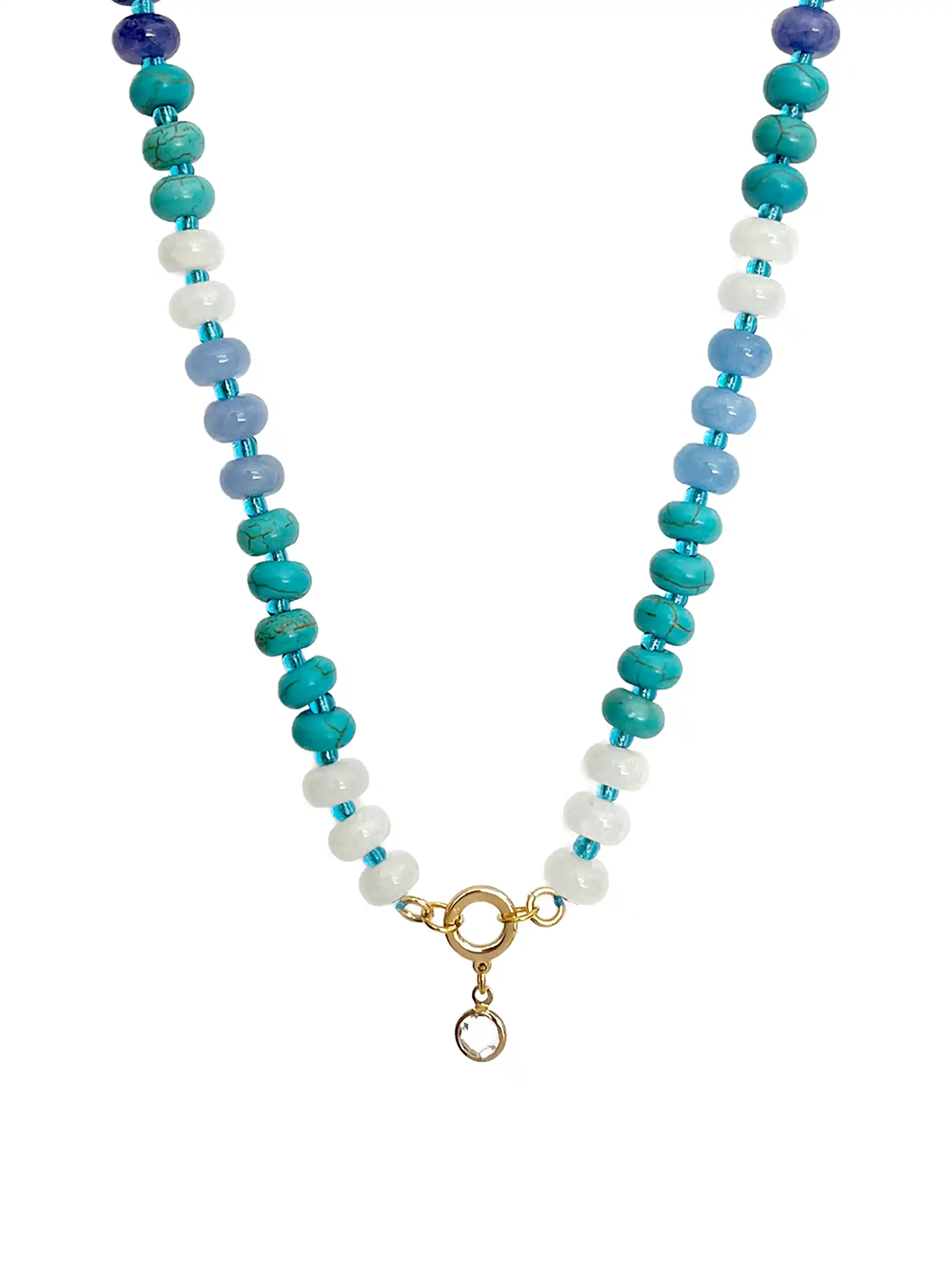 A top-down photograph of a unique handmade semi-precious stone beaded necklace against a white background. The necklace features alternating deep blue, turquoise, light blue, and white stone beads. At the center is a gold-colored round ring with a small, clear crystal point pendant hanging from it.