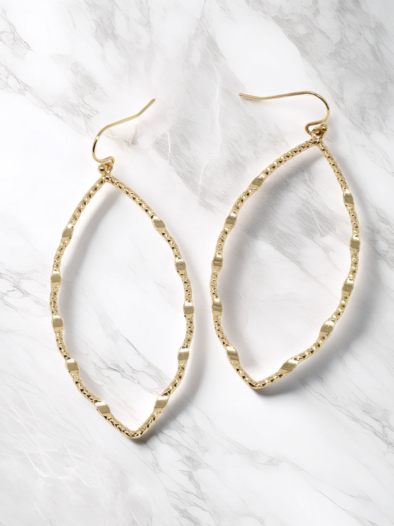 A close-up view of a pair of gold drop statement earrings with marquise-shaped drop that feature a textured metal surface. The earrings are suspended from small gold hooks and would add a touch of glamour and sophistication to any outfit.