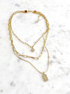 A triple-layered gold necklace featuring various chains adorned with modern, paved charms.
