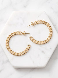 Gold chain-link hoop earrings displayed on a white hexagonal marble tray over a light marble surface.