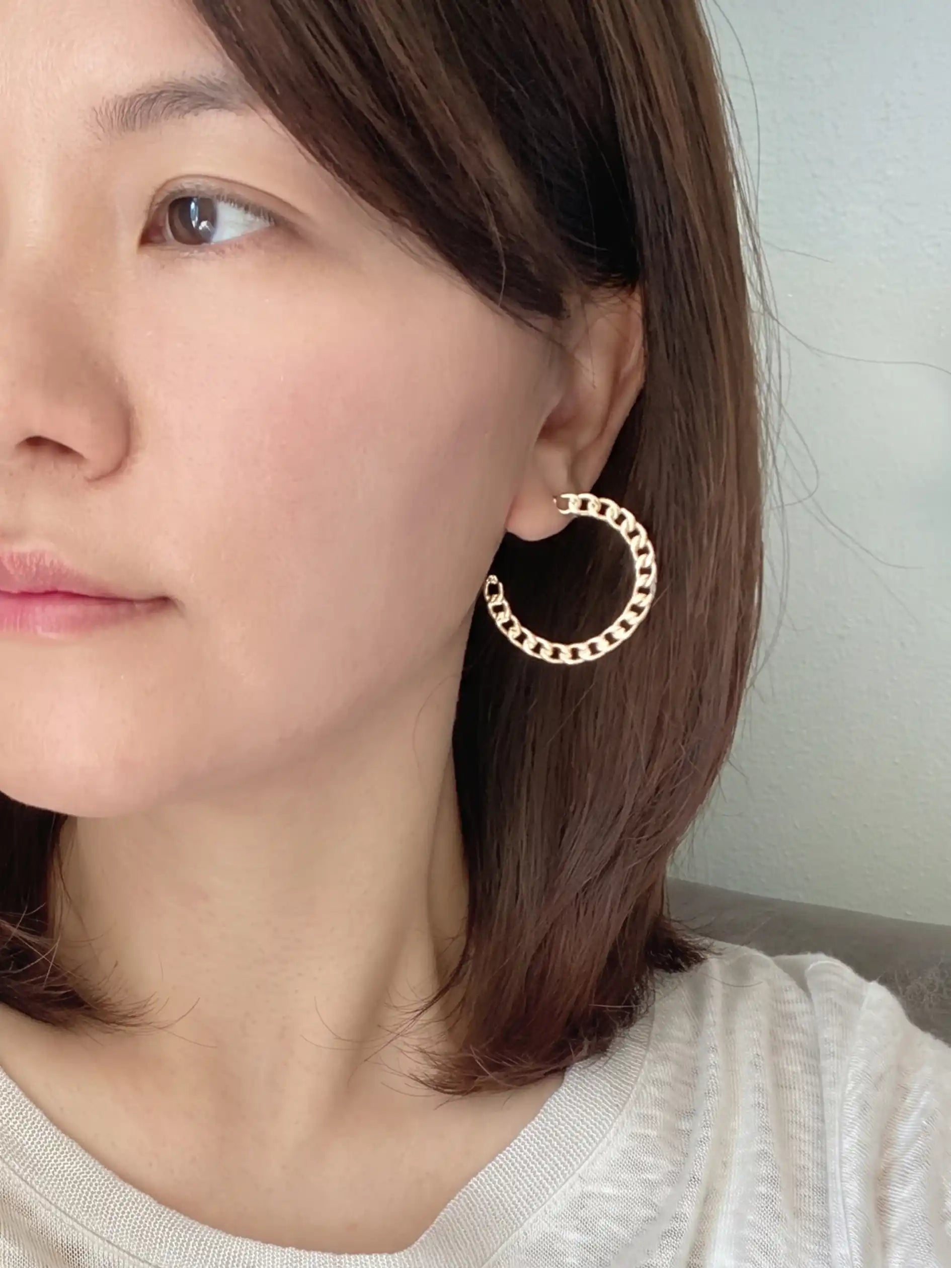 A close-up of a woman wearing a large gold hoop earring with small black dot accents, set against a soft, neutral indoor background.