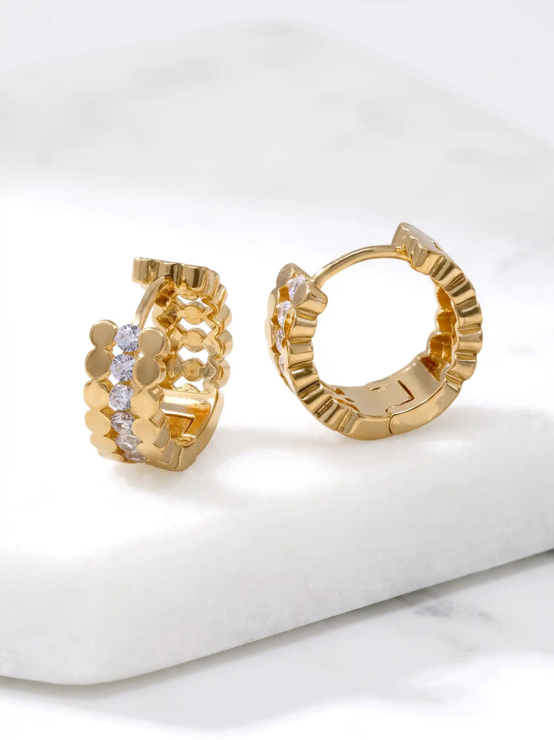 Close-up of a pair of thick, bold gold-filled huggie hoop earrings embedded with sparkling crystals.