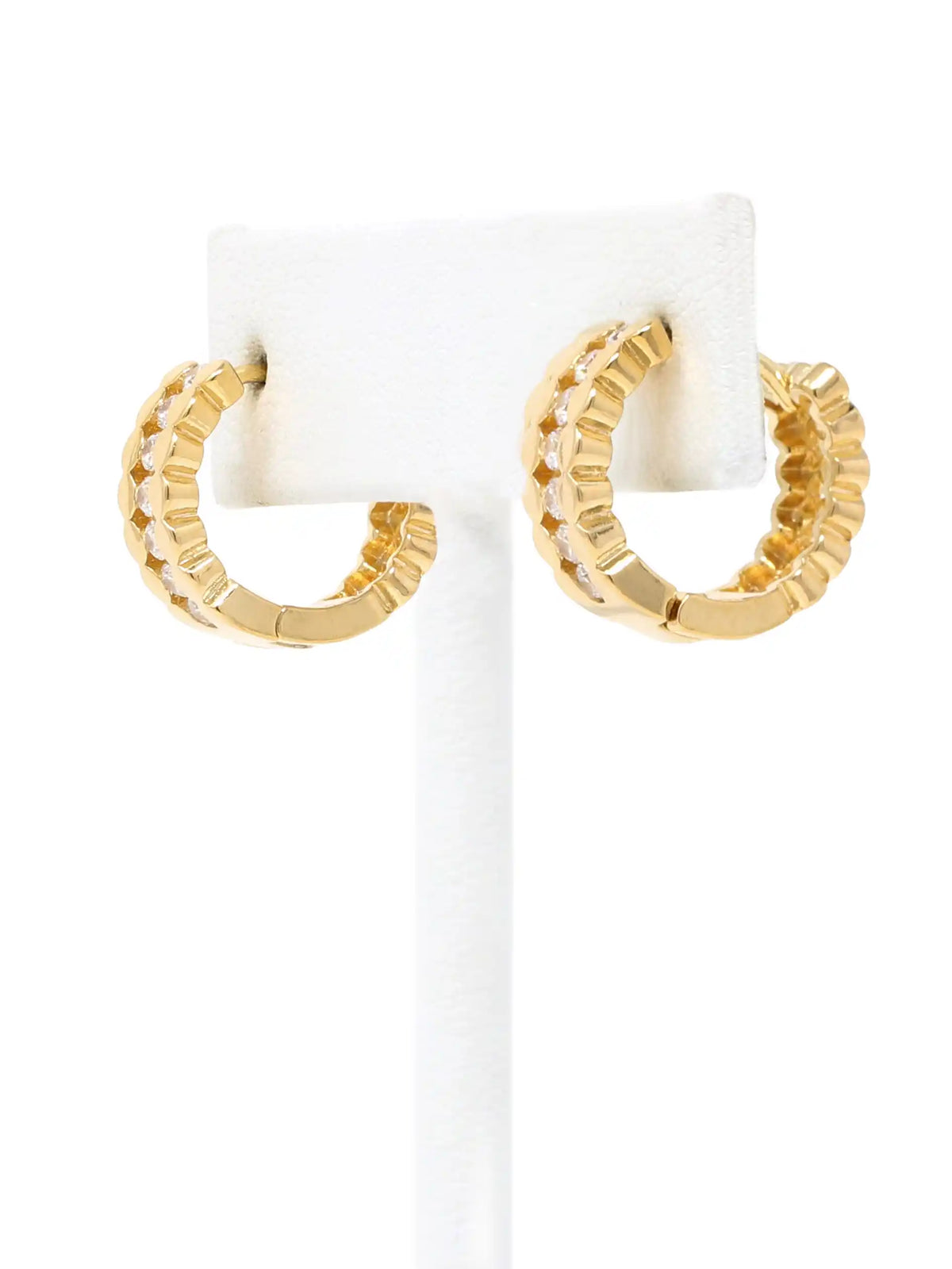 A pair of gold huggie hoop earrings with a textured, ridged outer edge and small clear stones along the inner curve, displayed on a white jewelry stand against a white background.