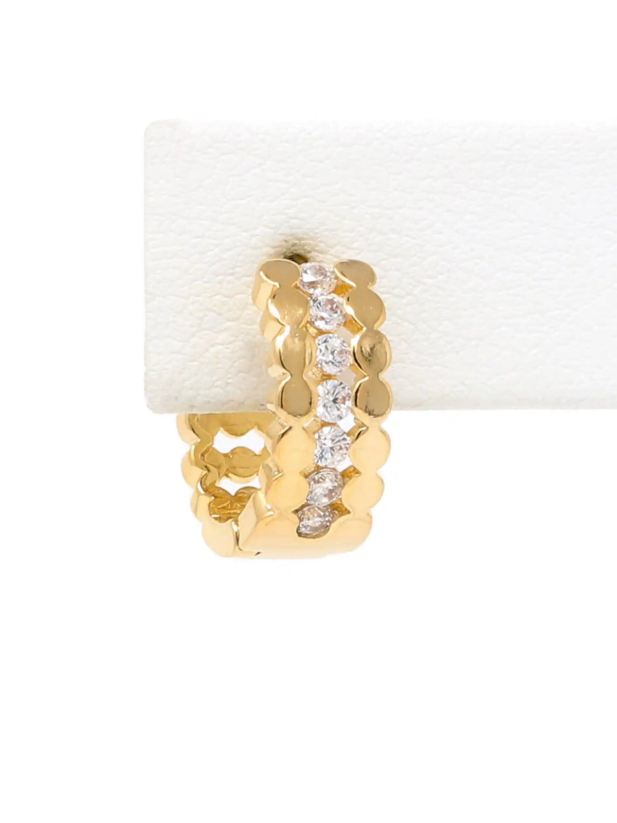 A gold huggie hoop earring with a vertical channel of clear pavé-set stones, displayed on a white textured jewelry stand against a white background.
