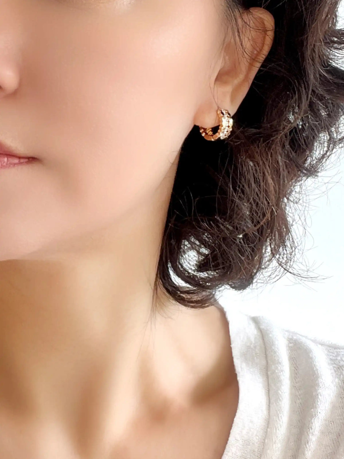 A close-up of a woman's ear wearing a small gold crescent moon hoop earring with sparkling clear stones.