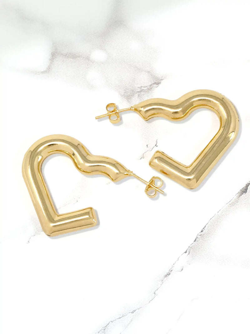 A pair of gold-toned, wavy open heart-shaped hoop earrings with post-back closures, displayed on a white marble surface.