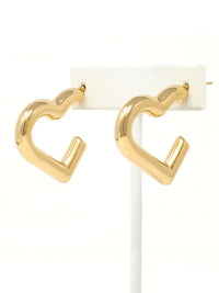 A pair of gold-toned, open heart-shaped hoop earrings displayed on a white jewelry stand against a white background.