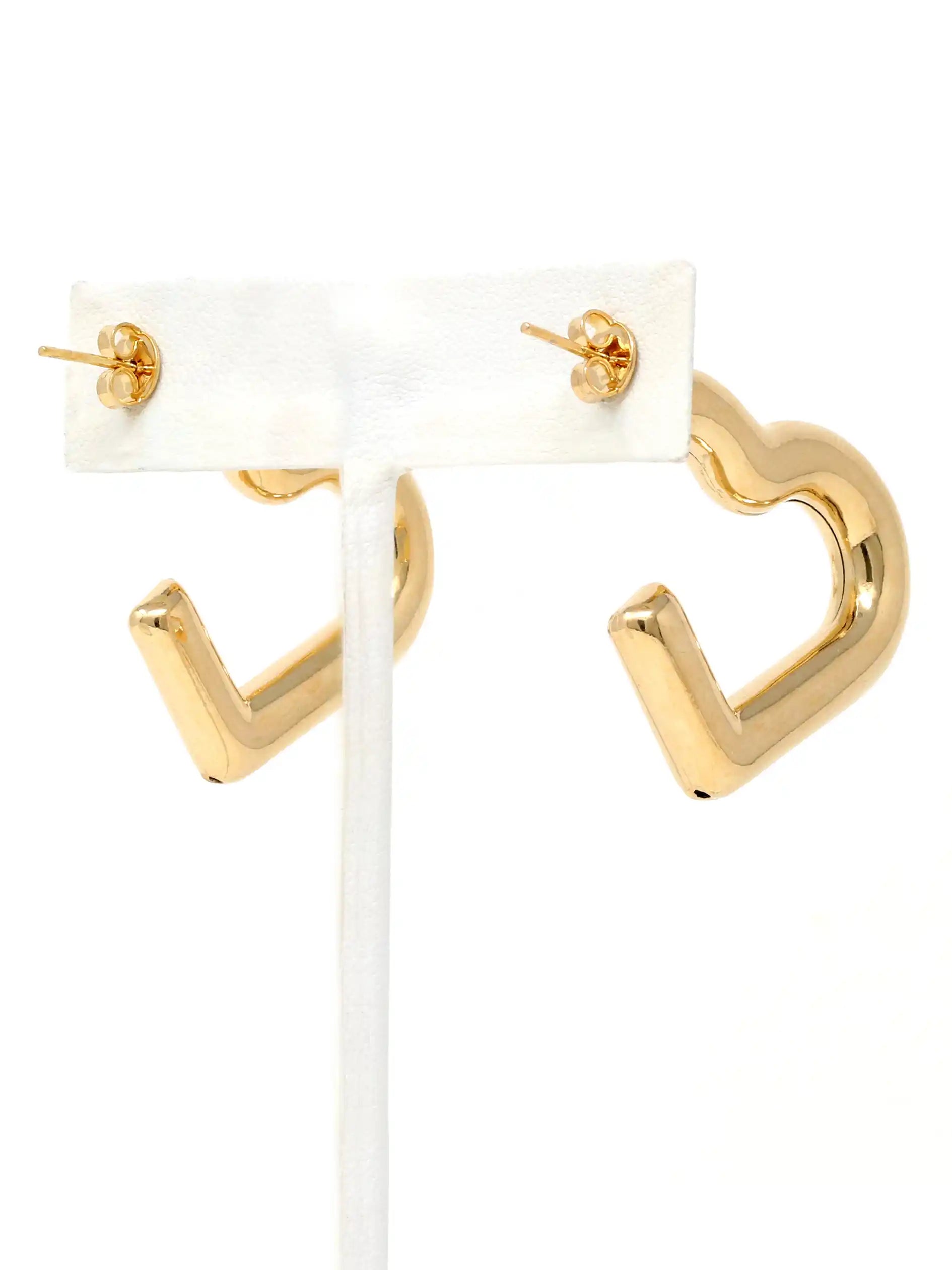 Gold geometric hoop earrings with a hollow heart design, displayed on a white jewelry stand against a white background.