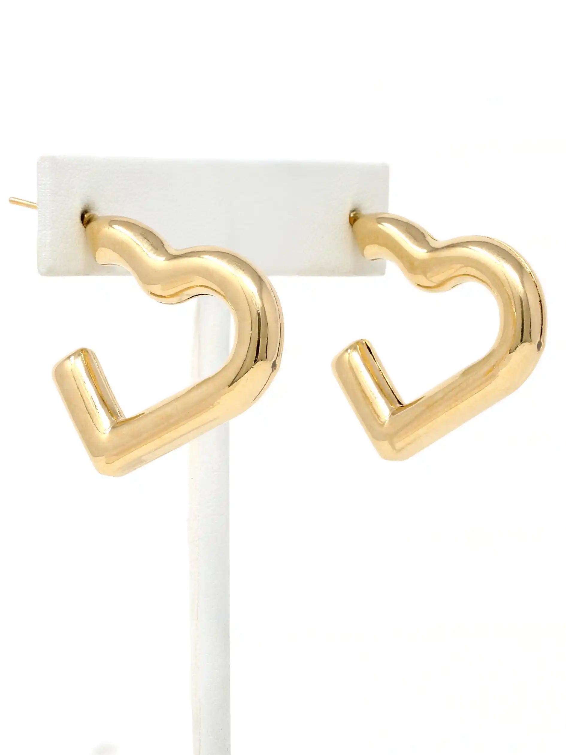 Gold heart-shaped hoop earrings displayed on a white jewelry stand against a white background.