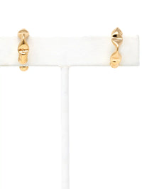 A pair of gold cuff hoop earrings with a twisted, organic wavy design, displayed on a white jewelry stand against a white background.