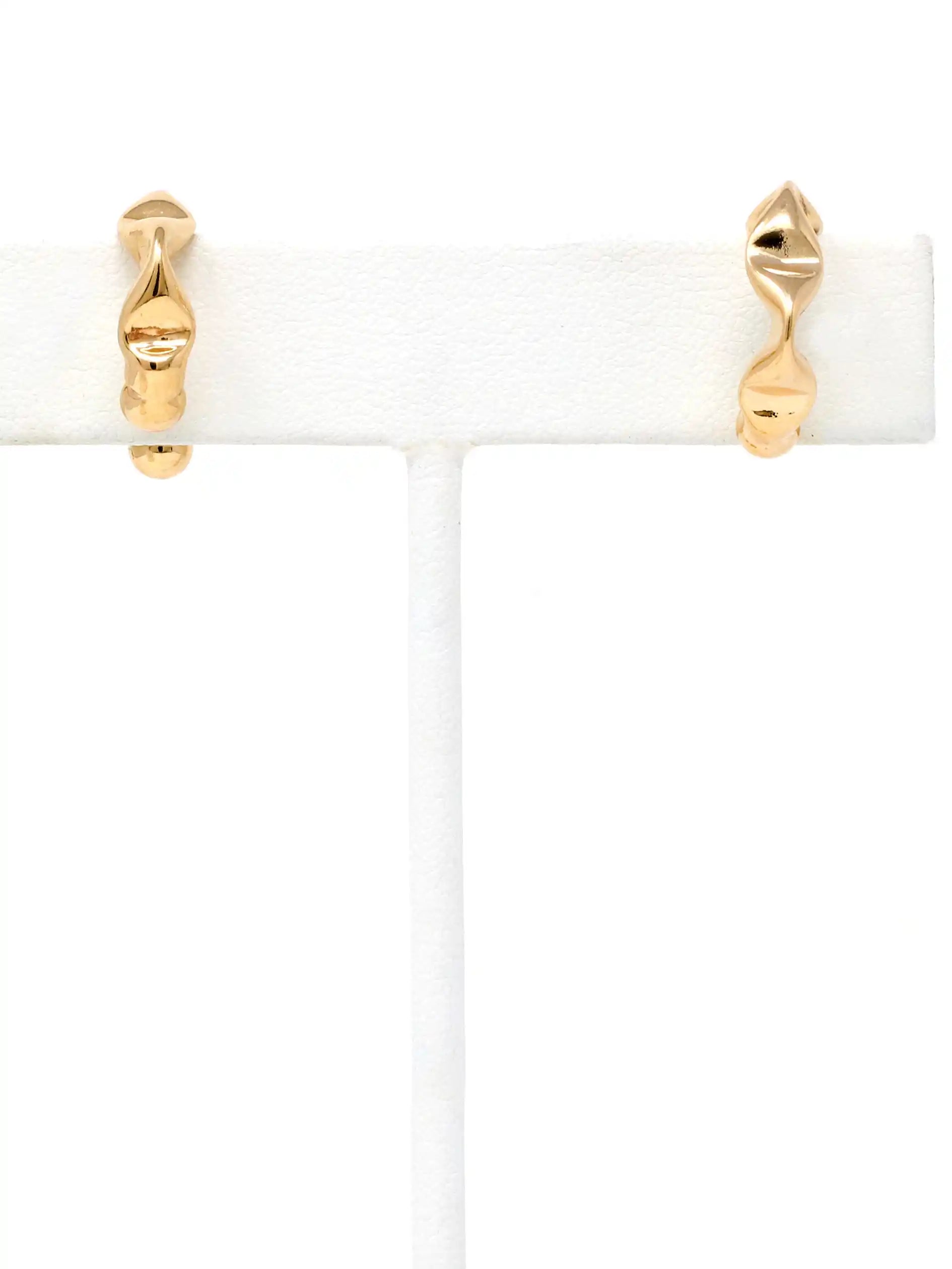 A pair of gold cuff hoop earrings with a twisted, organic wavy design, displayed on a white jewelry stand against a white background.