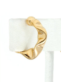 A pair of gold cuff hoop earrings with a twisted, organic wavy design, displayed on a white jewelry stand against a white background.