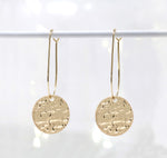 Lightweight metal hoop earrings in gold with small hammered circle charms.