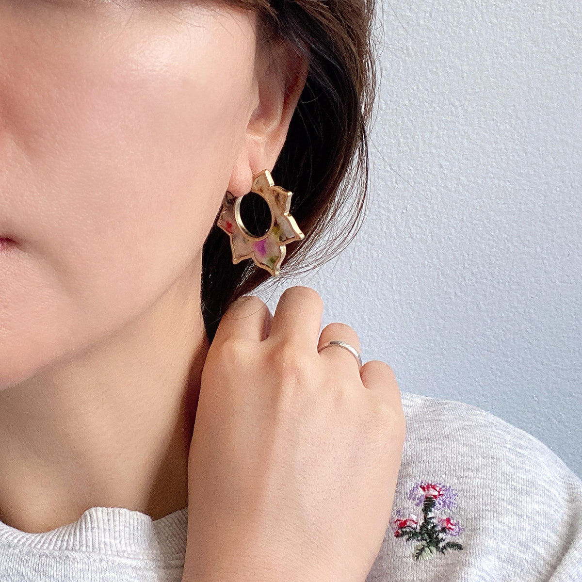 A pair of flower-shaped hoop earrings made of multicolored resin with a gold-tone outline.