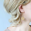 wearing of lightweight metal hoop earrings in gold with small hammered circle charms.