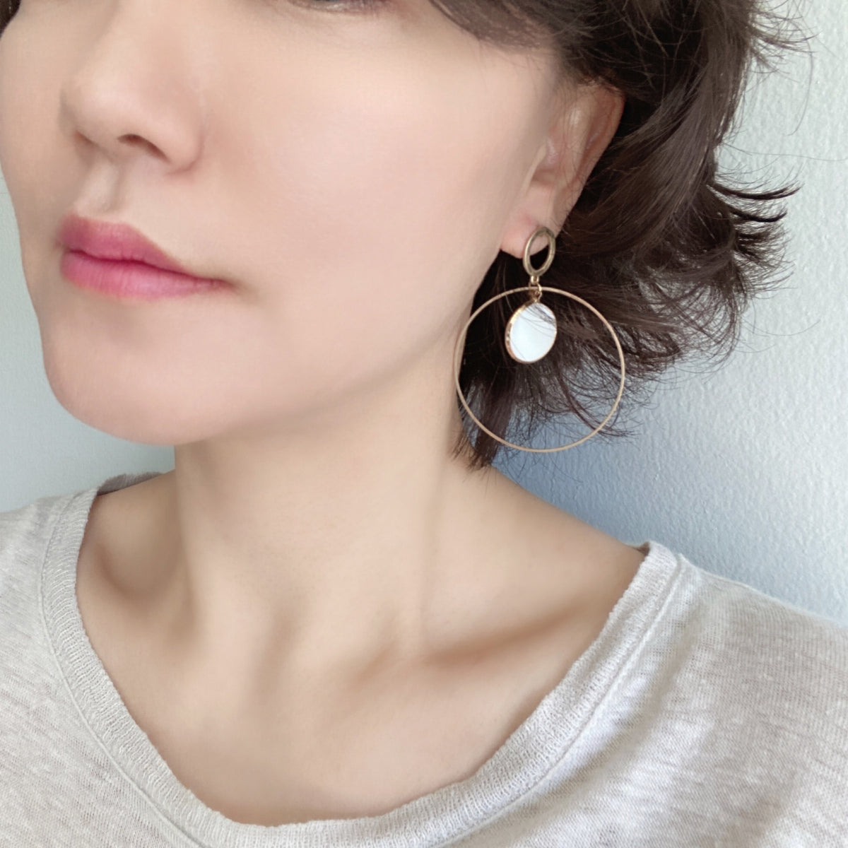 A pair of gold-tone dangle hoop earrings with round mother-of-pearl inlays. The earrings feature a modern, lightweight design with a circular stud and push-back closure.