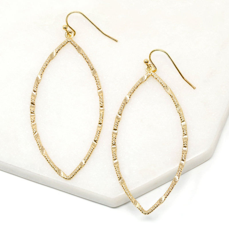 A close-up view of a pair of gold drop statement earrings with marquise-shaped drop that feature a textured metal surface. The earrings are suspended from small gold hooks and would add a touch of glamour and sophistication to any outfit.