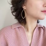 A close-up view of a pair of gold drop statement earrings with marquise-shaped drop that feature a textured metal surface. The earrings are suspended from small gold hooks and would add a touch of glamour and sophistication to any outfit.