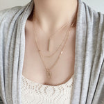Wearing a modern triple-layered necklace in gold dangled with two bar charms.
