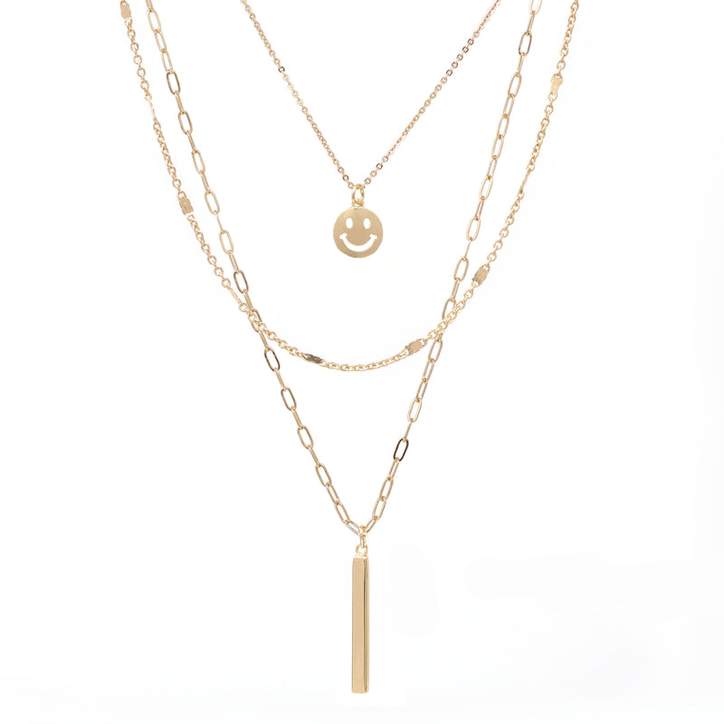 A set of triple layered necklace in gold with a small smiley face and a skinny bar charms.